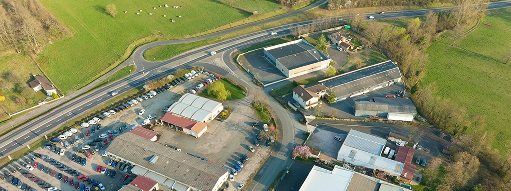 Vue aérienne d'une zone d'activités avec des hangars et entrepôts. Une route sépare cette zone de champs agricoles.